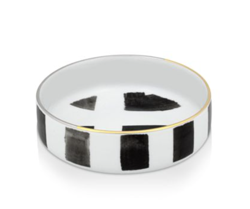 The Sol Y Sombra charger by Christian Lacroix x Vista Alegre is a round white porcelain piece with a thin gold rim and striking black abstract geometric shapes—an elegant dinnerware item from Vista Alegre.