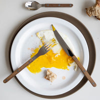 A white plate with a partially eaten fried egg and bread, featuring the Sabre Bistro Flatware 5 Piece Setting - Teak fork and knife on the plate. A spoon from the set and more bread sit beside the plate.