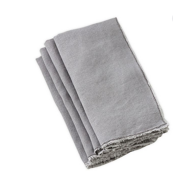 The Saro Trading Fringe Stone Washed Napkin Grey Set of 4 features light gray linen napkins with fringe edges, neatly folded and stacked on a white surface.