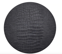 The Kim Seybert Croco Placemat Charcoal Set of 4 features a round, black surface with a textured, crocodile-embossed pattern resembling reptile skin, showcased against a white background.