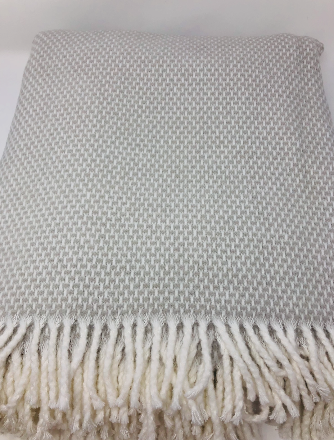 The Grain of Rice Throw by A Soft Idea, in grey and white houndstooth with a cream fringe, is shown neatly folded on a plain white background.