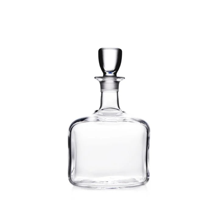 The Simon Pearce Woodbury Decanter features handblown glass, a round stopper, wide square base, and narrow neck—perfect for elevating your home bar. Shown on a white background.