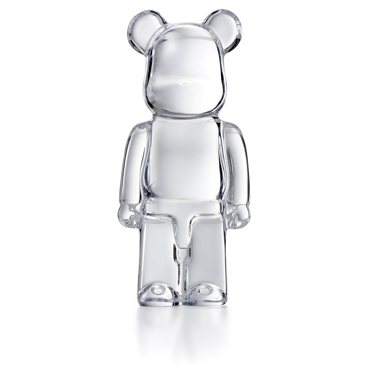 The Bear Brick by Baccarat is a luxury collectible art toy with a transparent, glass-like finish and rounded ears, shown standing on two legs against a plain white background.