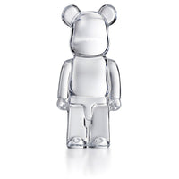 The Bear Brick by Baccarat is a luxury collectible art toy with a transparent, glass-like finish and rounded ears, shown standing on two legs against a plain white background.
