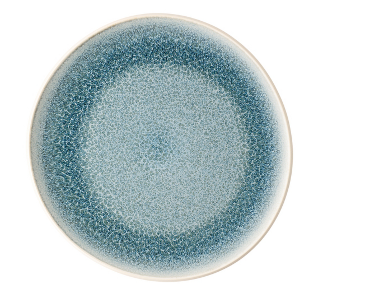 The Rosenthal Junto Aquamarine Dinnerware features a round ceramic plate with a mottled blue reactive glaze, fading from dark at the rim to lighter blue in the center, set against a white background.