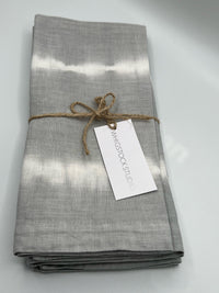 A set of four hand dyed linen napkins in Pebble by Whigstock Studio, folded and tied with brown twine and a branded tag, adds an elegant, sustainable touch to your table setting.