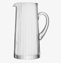 The LSA Aurelia Jug is a classic pitcher made from mouth-blown glass, featuring vertical ridges, a curved handle, and a small spout. It is shown against a plain white background.