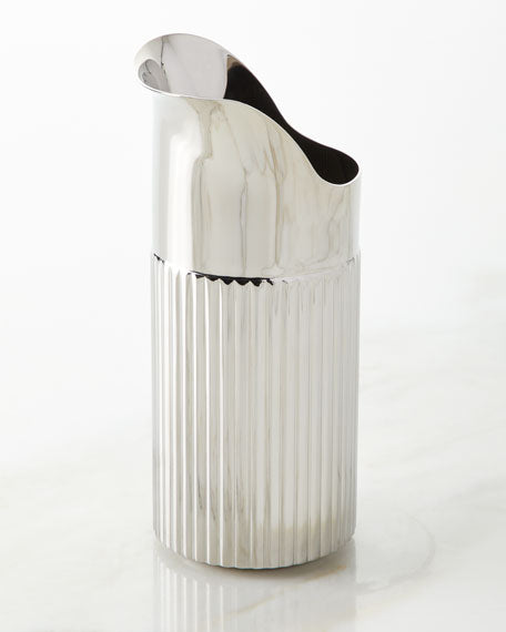 The Georg Jensen Bernadotte Stainless Creamer features a tall, silver design with vertical ribbing on the lower half and a smooth curved spout, shown on a light-colored surface.