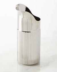 The Georg Jensen Bernadotte Stainless Creamer features a tall, silver design with vertical ribbing on the lower half and a smooth curved spout, shown on a light-colored surface.