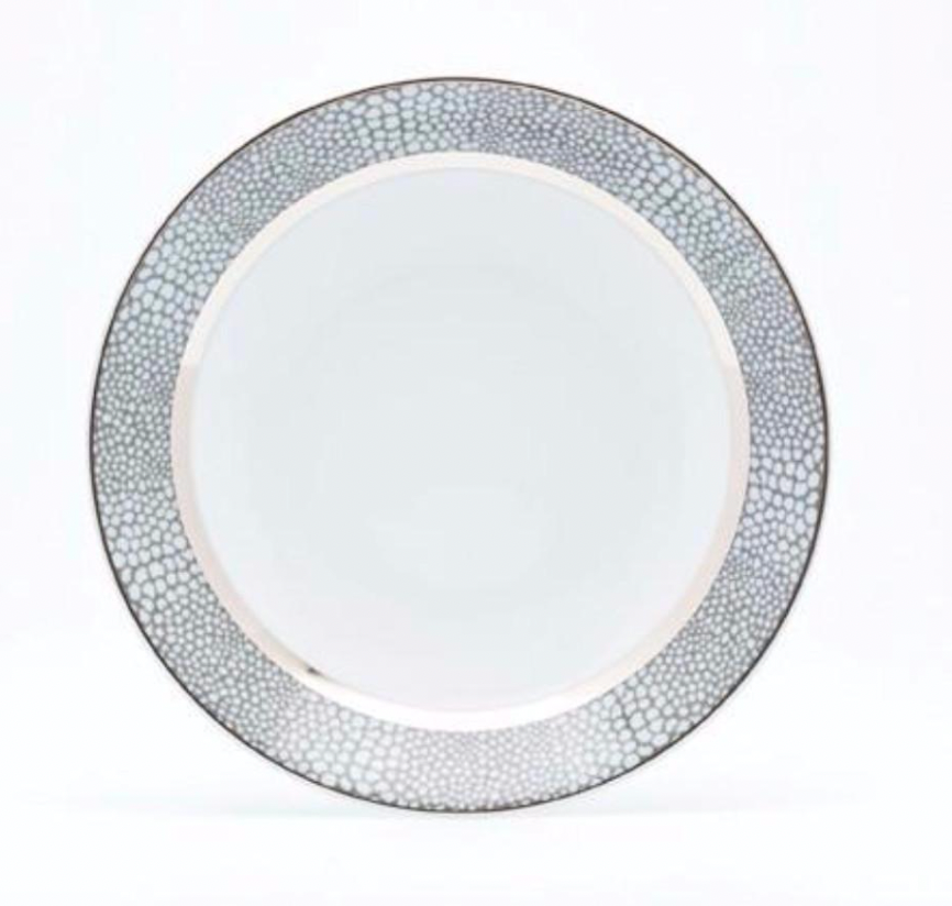 The Makassar Gray & Platinum Dinnerware by Royal Limoges/Bia Cordon Bleu features a round white plate with a platinum, pebble-like textured rim and smooth center, handcrafted in France from fine Limoges porcelain. Background is white.
