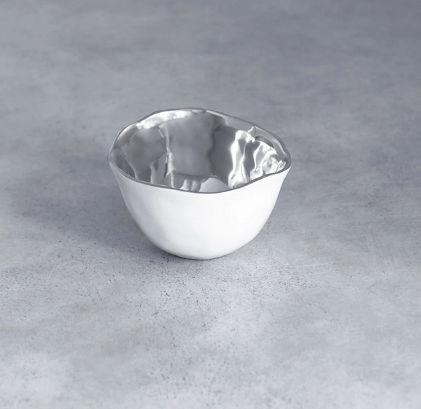 The Thanni Osaka Bowl White and Silver Small by Beatriz Ball is a small, uniquely shaped serving bowl featuring a shiny silver finish, displayed elegantly on a smooth gray surface.
