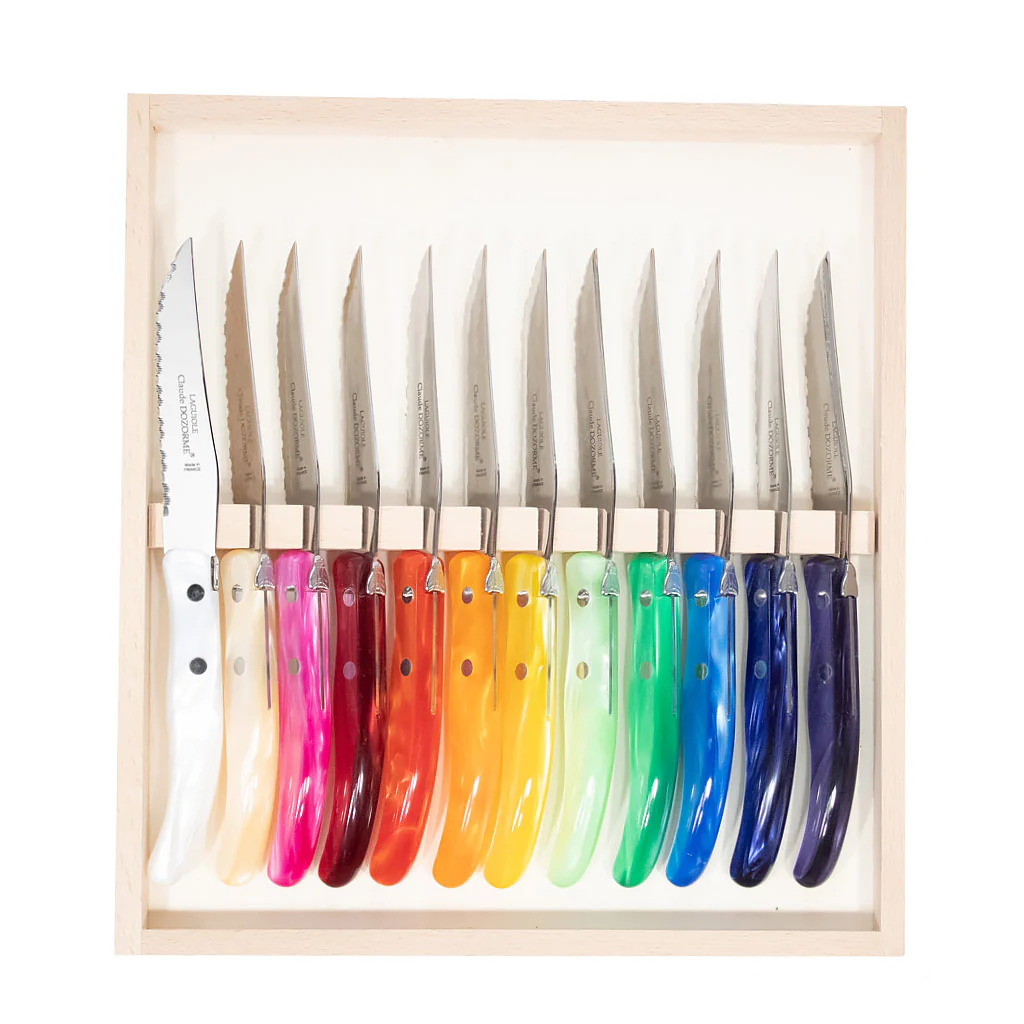 The Claude Dozorme Berlingot Assorted Steak Knives Set of 12 features stainless steel blades, gradient colorful handles from white to dark blue, and comes in a light wooden box. Made in France.