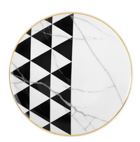 The Carrara by Coline Le Corréa Dinnerware from Vista Alegre features a round porcelain plate with a gold rim, white Carrara marble pattern, and black and white geometric triangles reflecting French designer elegance.