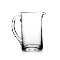 The Simon Pearce Ascutney Pitcher Medium is a handmade clear glass pitcher with a curved handle and spout, shown empty against a white background.