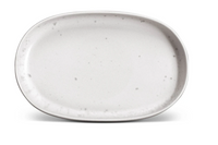 The L'Objet Terra Stone Dinnerware plate is an empty oval-shaped, hand-crafted porcelain plate in light gray with dark speckles, shown on a white background.