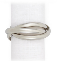 A white textured napkin is vertically displayed against a white background, wrapped with a silver-tone Three Ring Jewel Napkin ring from L'Objet’s Napkin Set of 4.
