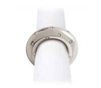 A round, silver Stars Napkin Jewels napkin ring by L’Objet holds a white cloth napkin against a plain white background.