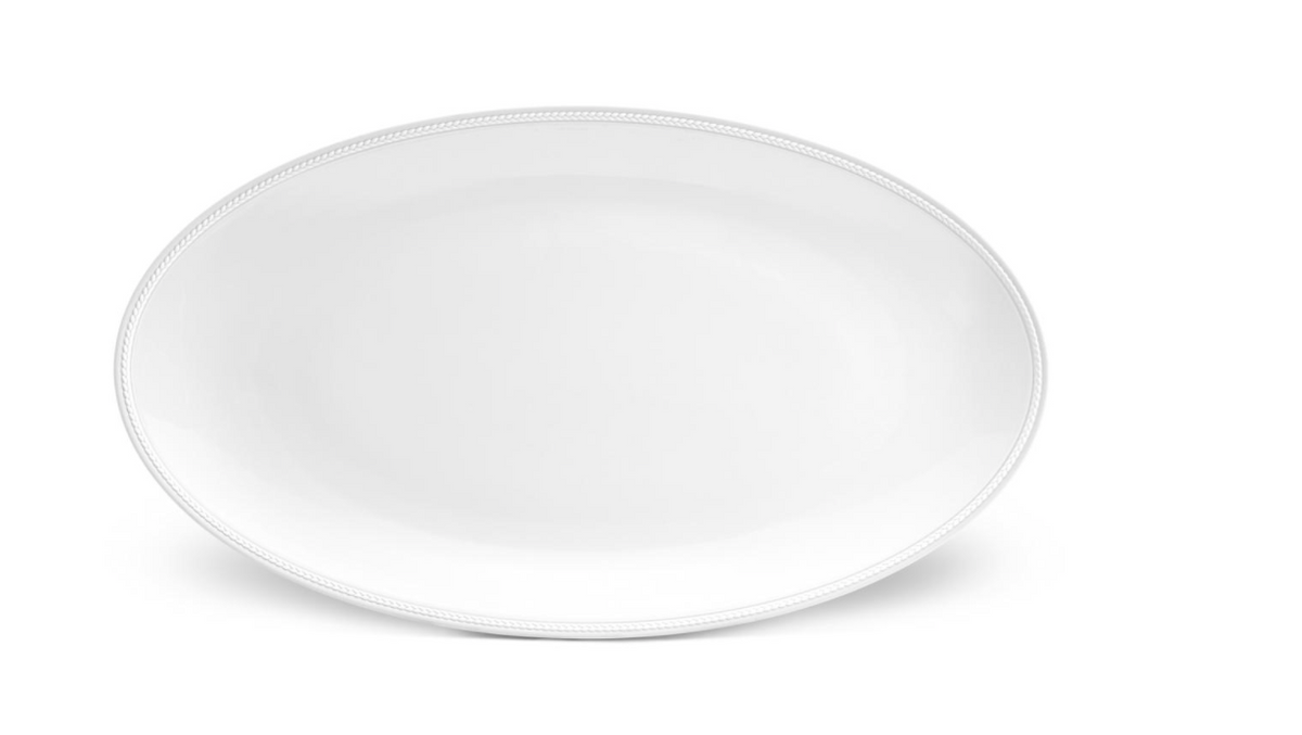 The Soie Tressée White Dinnerware by L'Objet features a large, oval ceramic dinner plate with a subtle textured rim, shown against a white background.
