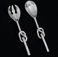 The Knotty Salad Set by Inspired Generations features a fork and spoon, each handcrafted from polished aluminum with twisted knot handles, beautifully displayed on a black background.