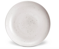 The L'Objet Terra Stone Dinnerware plate features a round shape, light gray matte finish, and subtle speckles, reflecting handcrafted elegance. Photographed from above on a white background.