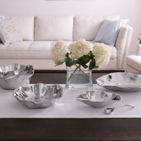 A living room with a beige sofa, light blue pillows, a glass vase of white hydrangeas, and a dark wood table set with five Beatriz Ball Vento Claire Bowls with Spoon on a white runner.