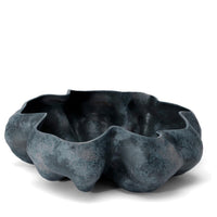 Dark, irregularly shaped Timna Bowl Blue by L’Objet features wavy edges and a textured surface reminiscent of natural stone—evoking the raw beauty of King Solomon’s Mines—set against a plain white background.