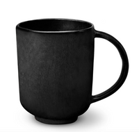 A matte black ceramic mug with a large curved handle, shown on a white background. From L'Objet's Terra Iron Dinnerware collection, the mug boasts a simple modern design with smooth surfaces and no decoration.