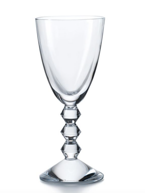 The Baccarat Vega White Wine Glass features a clear, faceted design with a geometric diamond-shaped stem and wide bowl, showcased against a plain white background.