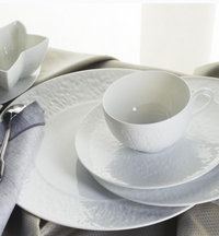 The Raynaud Mineral Dinnerware Glazed White set—featuring Limoges porcelain cup, saucer, and plates—is displayed on a light cloth with silver cutlery beside it.