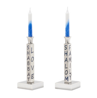 The Shabbat Candlestick Set/2 by Inspired Generations features two silver holders, each with blue-and-white candles and blue "SHABBAT" and "SHALOM" inscriptions—ideal for a meaningful, welcoming table setting.