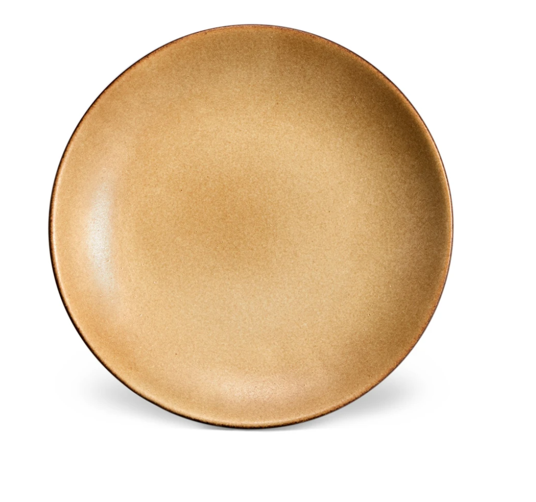 The Terra Leather Dinnerware by L'Objet is a hand-crafted, round ceramic plate in light brown with a smooth matte finish, shown against a white background.