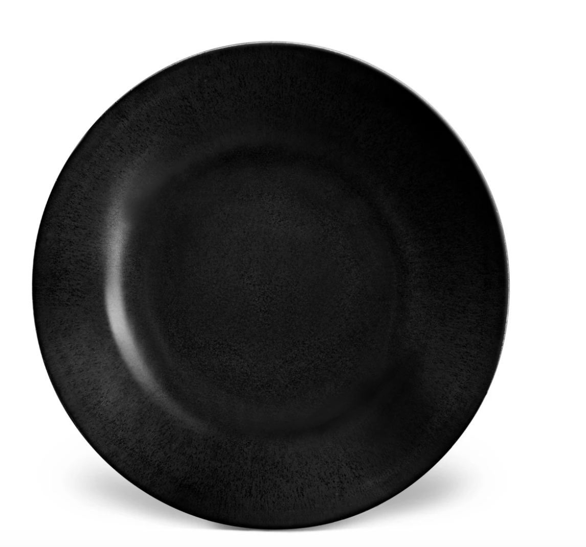 An empty, round, matte black ceramic plate from the Terra Iron Dinnerware collection by L'Objet sits centered on a white background. The handcrafted plate features a subtly textured surface.