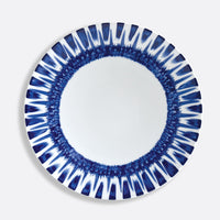 The Bernardaud In Bloom Dinnerware features a round white porcelain plate adorned with a bold blue geometric pattern of brushstroke-like lines radiating along the rim in a striking circular design.