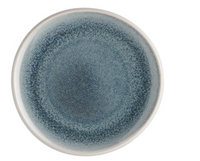 The Rosenthal Junto Aquamarine Dinnerware features a round ceramic plate with a white rim and textured blue gradient center, created with reactive glaze for a unique watercolor effect. This stoneware is dishwasher and microwave safe. Background is white.