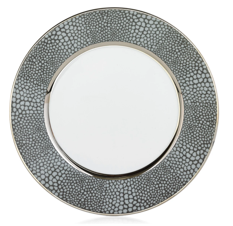 The Makassar Gray & Platinum Dinnerware by Royal Limoges/Bia Cordon Bleu features a round ceramic plate handmade in France, with a plain white center, wide textured gray rim with small spots, and thin platinum bands for an elegant touch.