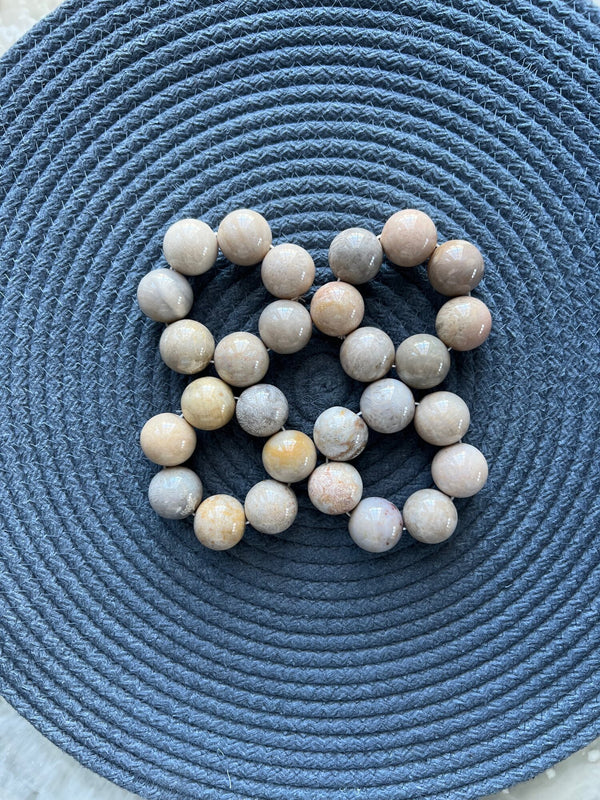 A set of four Marble Bead Napkin Rings in cream by Whigstock Studio is arranged in a square on a textured, circular dark gray woven mat.