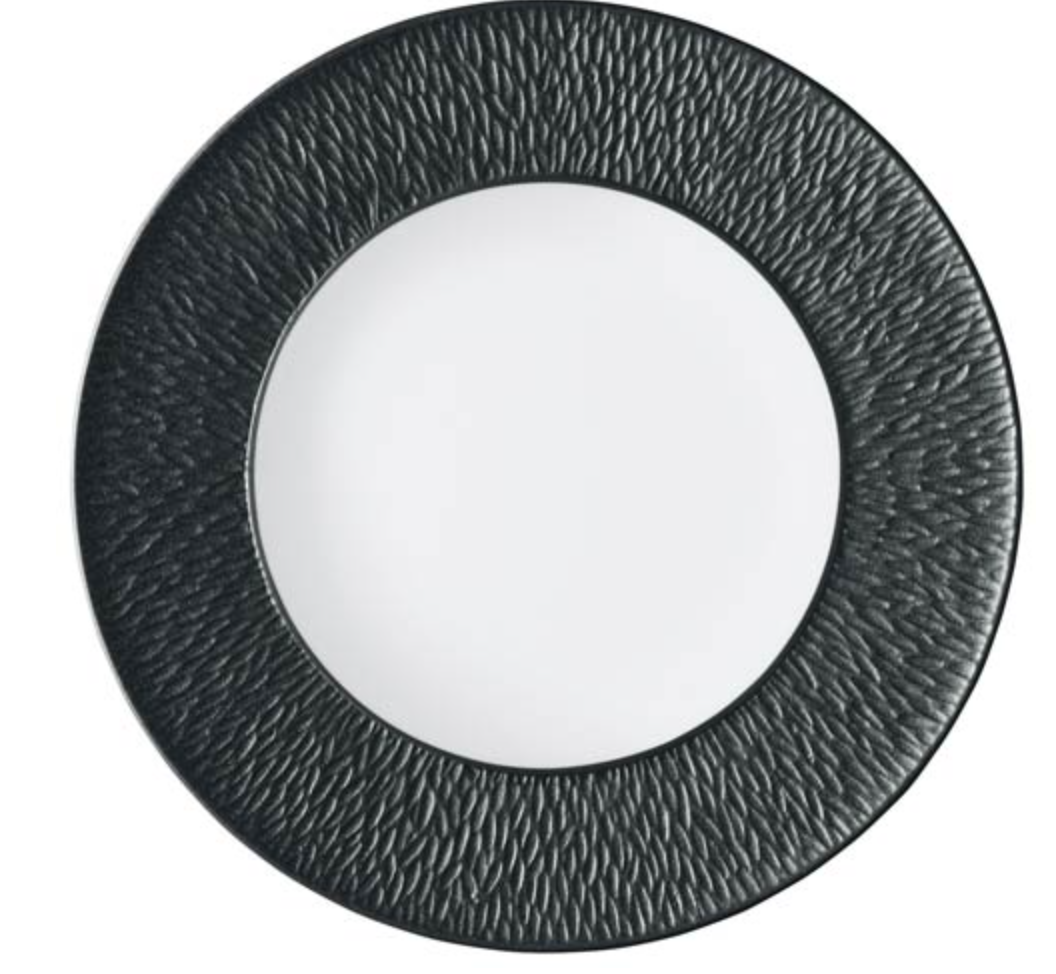 The Mineral Irise Dinnerware - Black by Raynaud features a smooth white center and a wide, textured black rim with a subtle wavy pattern. Made from Limoges porcelain, it offers a modern, minimalistic design perfect for contemporary tables.