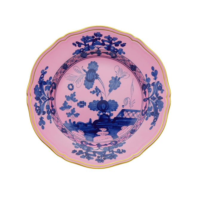 The Oriente Italiano Dinner Plate Azalea by Ginori 1735 features a scalloped edge, yellow rim, and a pink background adorned with intricate blue floral and landscape designs in the center and along the border.