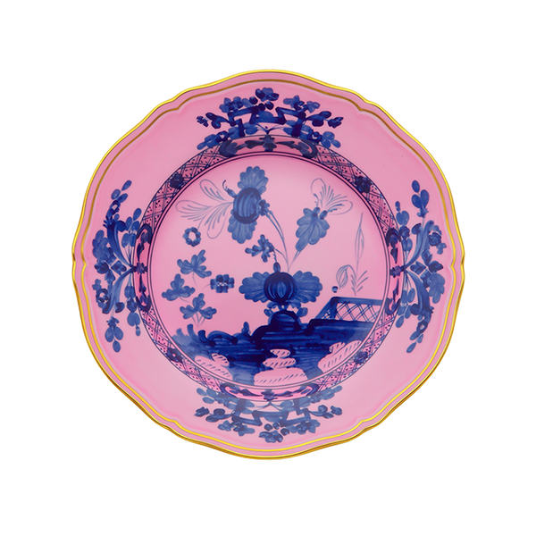 The Oriente Italiano Dinner Plate Azalea by Ginori 1735 features a scalloped edge, yellow rim, and a pink background adorned with intricate blue floral and landscape designs in the center and along the border.