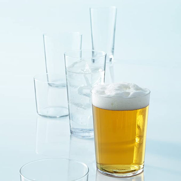 A clear glass of beer sits in the foreground, while empty and partially filled LSA Gio Tumbler Large Set of 4—stackable tumblers for everyday use with water and ice—are arranged on a reflective surface in the background.