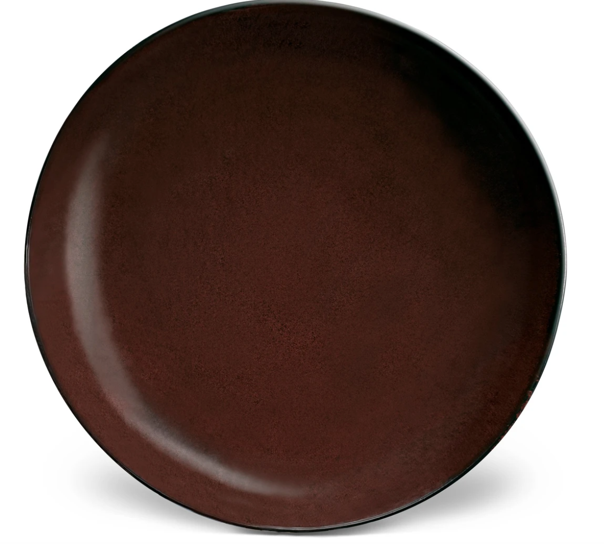 The L'Objet Terra Wine Dinnerware plate is large and round, featuring a deep brown, slightly textured surface with a subtle glossy finish. It is beautifully photographed against a white background.