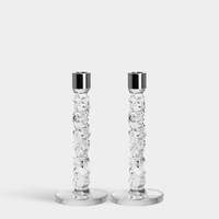 The Orrefors Kosta Boda Carat Candlesticks Silver Set of 2 features textured, faceted stems and smooth round bases with shiny silver candle cups, standing side by side on a plain white background.
