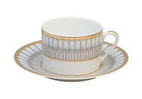 A white porcelain teacup and matching saucer featuring an ornate gold and gray geometric pattern and delicate gold trim, crafted in the classic style of Philippe Deshoulieres Arcades Gold Dinnerware.