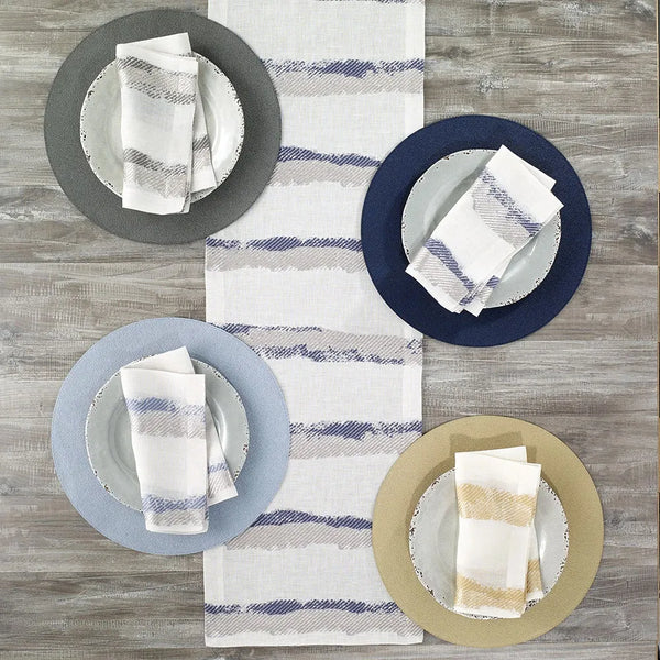 A wooden table is set for four with white plates, colorful chargers, and Bodrum’s Brushstroke Napkin Navy Set of 4—contemporary, easy-care linen polyester napkins—adding a stylish touch perfect for everyday meals.