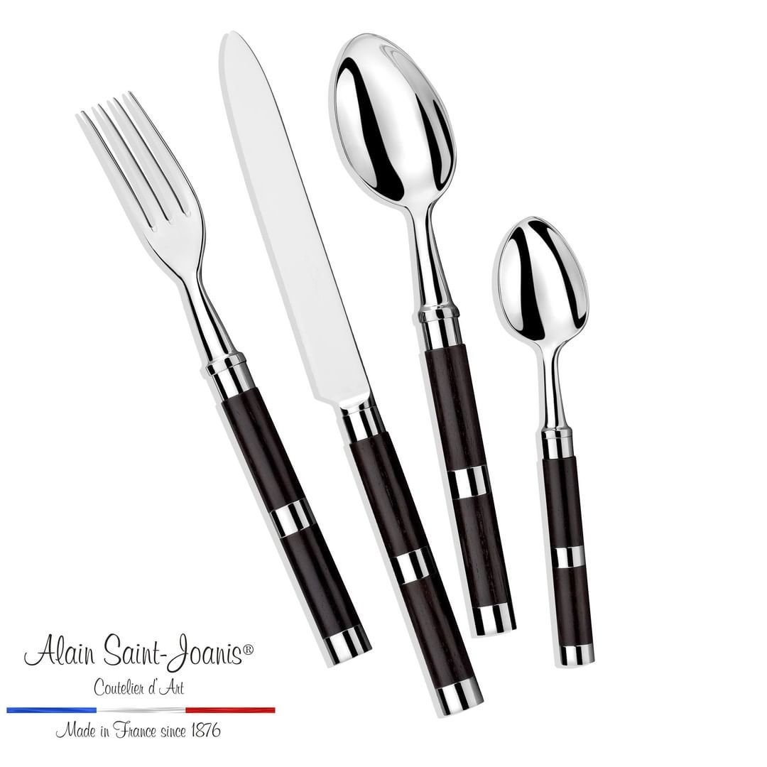 The Alain Saint-Joanis Carla Flatware Ebony 5 Piece Setting features hand-polished stainless steel utensils with dark handles, arranged side by side. Logo text: Alain Saint-Joanis flatware, hand-polished in France since 1876.