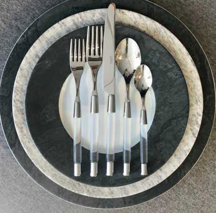 A Capdeco Zoe Flatware 5 Piece Setting - Clear is neatly arranged on three round plates with black and white marble patterns, viewed from above.