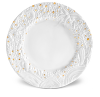 The Haas Mojave Dinnerware Gold plate by L'Objet features a white ceramic design with an embossed, textured rim showcasing various shapes and gold accents. Its smooth, plain center blends elegance with fine porcelain artistry.