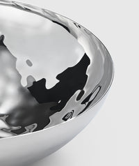 A close-up of the Mary Jurek Luna Serving Bowl 12" shows its polished, reflective stainless steel and smooth curved surfaces against a light grey background. This modern serving bowl is dishwasher safe.
