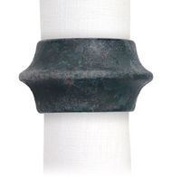 The Terra Cuff Napkin Ring Set of 4 by L'Objet features dark green, rustic metal rings with a wide, flared design, hand-crafted in Portugal and shown wrapped around a white textured cloth napkin.