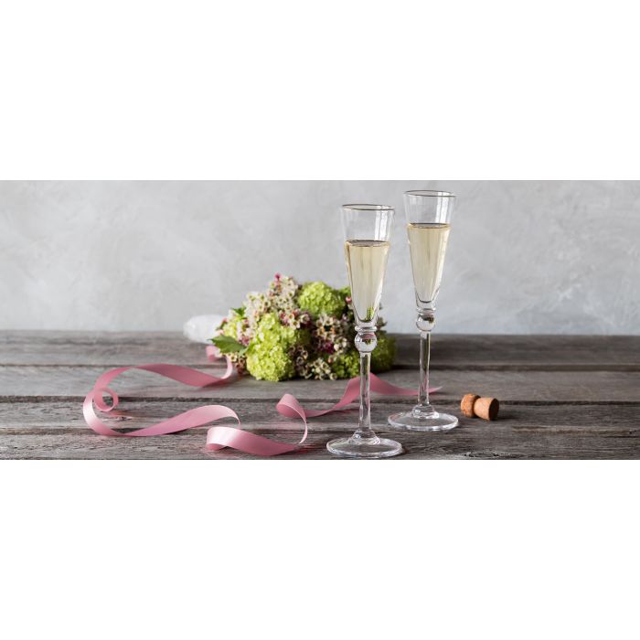 A pair of Simon Pearce Hartland Flute Set of 2 with sparkling wine on a wooden table, flowers and ribbon in the background—an elegant scene ideal for weddings or fans of handmade glassware.